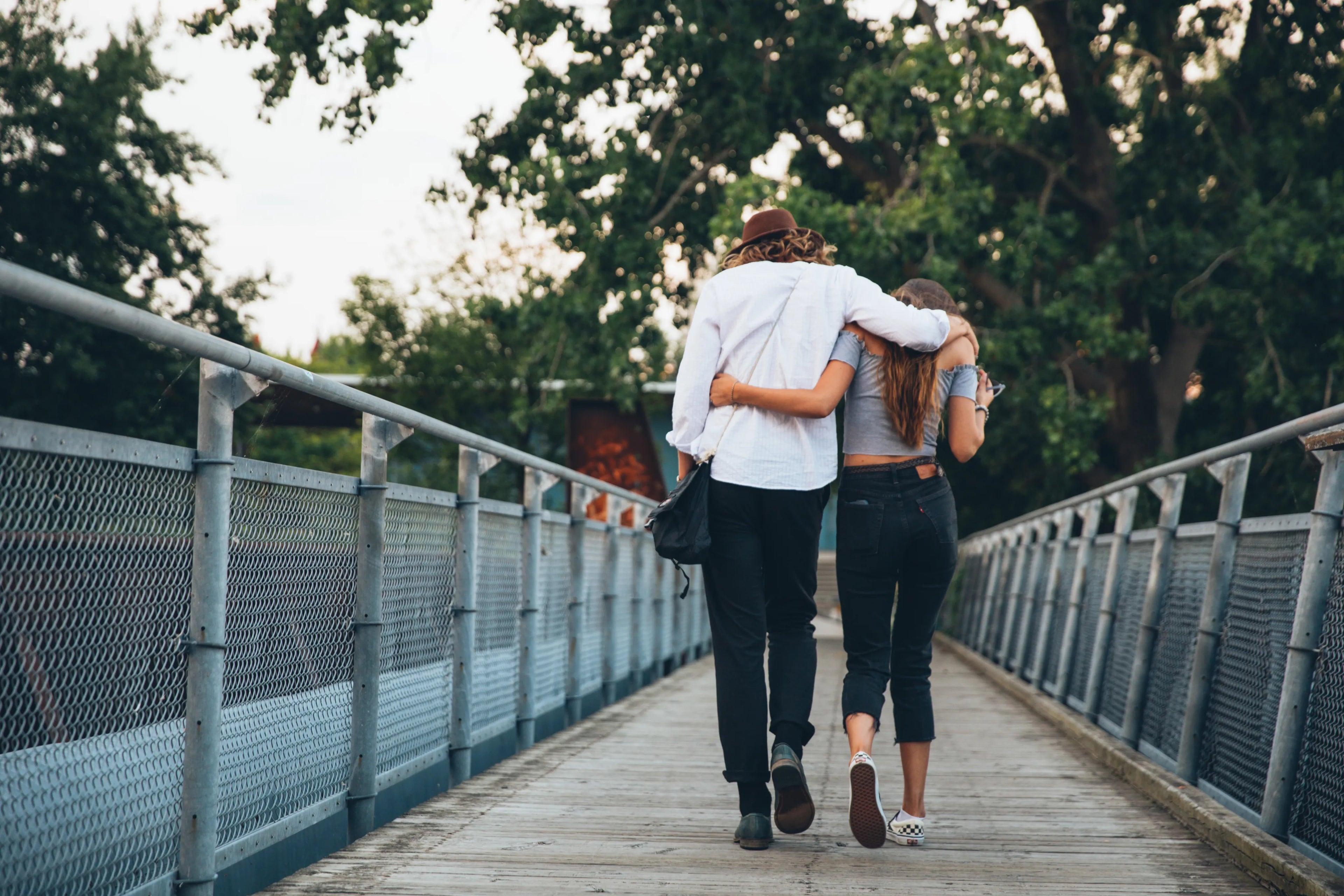 Two people walking arm-in-arm on a bridge with trees in the background
