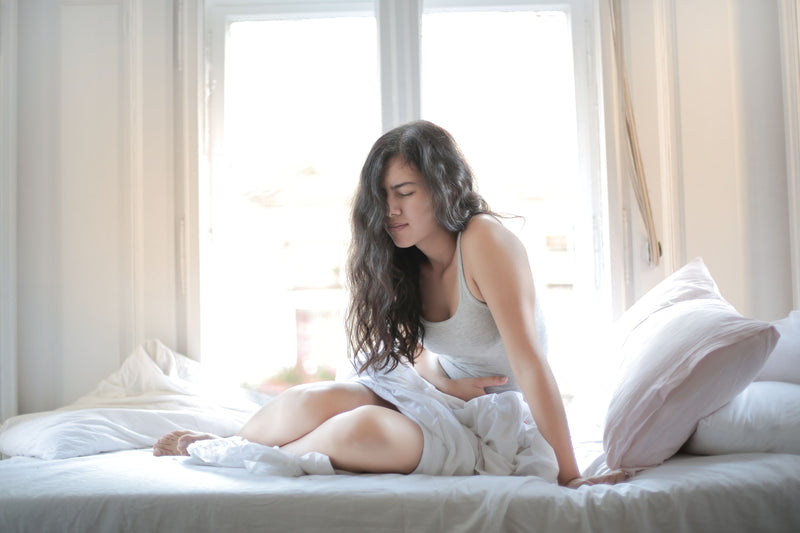Woman sitting on a bed in a bright room with large windows