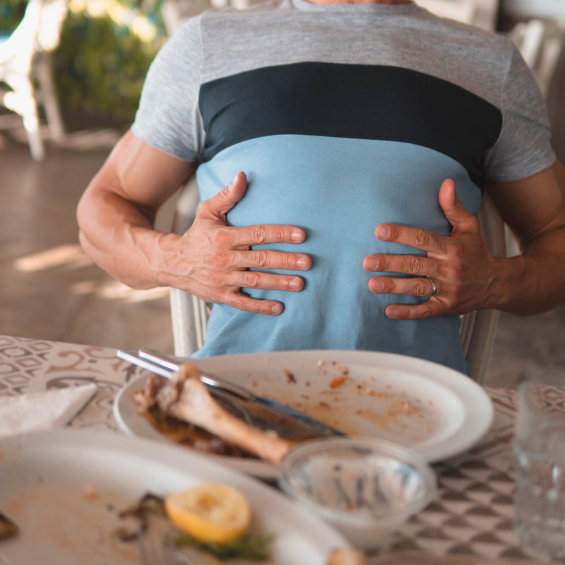 Man holding his belly at a dining table outdoors